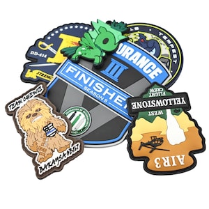 May include: A collection of colorful rubber patches with various designs and text. The patches include a Chewbacca character, a green pegasus, and text that reads "FINISHE SEASON 5", "YELLOWSTONE FLIGHT CREW", and "AIR3".