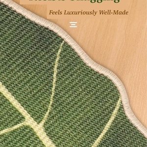 May include: Close-up of a green rug with a leaf pattern and a beige border. The text "Extra Durable Edge Resists Snagging" and "Feels Luxuriously Well-Made" is visible. The rug is on a wooden surface.