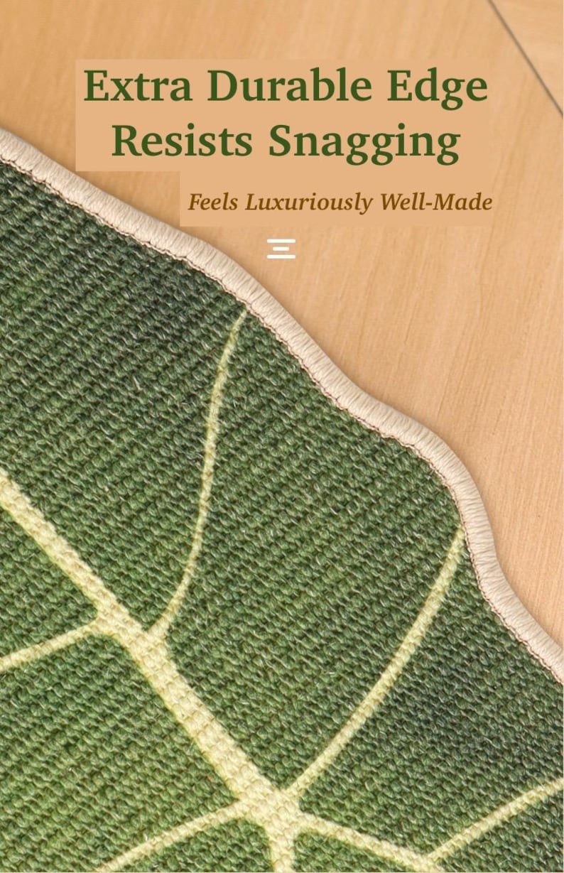 May include: Close-up of a green rug with a leaf pattern and a beige border. The text "Extra Durable Edge Resists Snagging" and "Feels Luxuriously Well-Made" is visible. The rug is on a wooden surface.