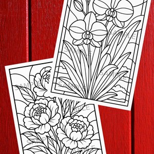 May include: Two black and white floral coloring pages featuring orchids and peonies. The images are in a stained glass style, with thick black outlines and the word "SAMPLE" printed on the pages. The background is a red wooden surface.