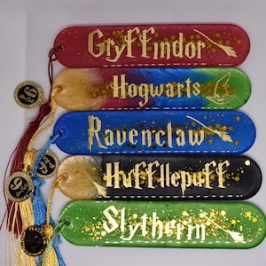May include: Five colorful resin bookmarks with gold lettering and accents. Each bookmark represents a Hogwarts house: Gryffindor, Hufflepuff, Ravenclaw, Slytherin, and Hogwarts. Tassels and charms are attached to the bookmarks.