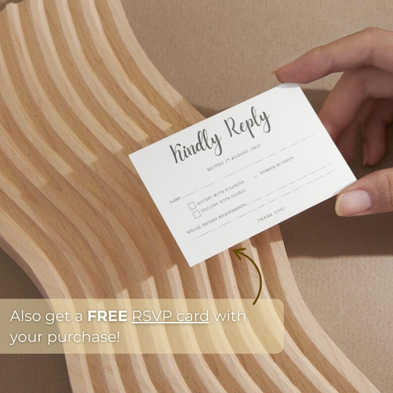 May include: A white RSVP card with the words "Kindly Reply" in elegant script. The card includes fields for name, acceptance, and dietary requirements. The card is held over a light-colored wooden surface.