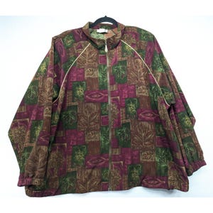 May include: A full-zip jacket with a leaf pattern in shades of brown, green, and burgundy. The jacket has a stand-up collar, long sleeves, and white trim along the zipper and shoulders. The jacket is hanging on a black hanger.