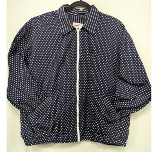 May include: Navy blue zip-up jacket with white polka dots. The jacket has a collared neckline with white pinstripes and a white zipper. The cuffs and hem are elasticized. The brand name "cev" is visible on the collar.