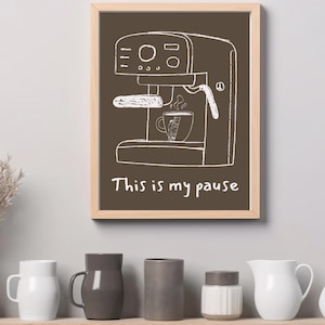 May include: A framed print featuring a white line drawing of an espresso machine on a brown background. The text "This is my pause" is below the machine. Several white and gray ceramic mugs and vases are on a shelf below the print.