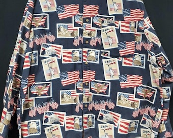 May include: A long-sleeved button-down shirt with a navy blue background. The shirt is patterned with American flags, eagles, and images of the Statue of Liberty and historical figures. The shirt has a collared neckline and a pocket on the chest.