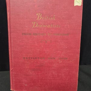 May include: A vintage book titled "British Dramatists" with gold lettering on a red cover. The book's title is prominently displayed, with the authors' names at the bottom. A small, faded sticker is on the upper right corner.