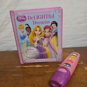Op de afbeelding: Een roze Disney Princess "Delightful Dreams" boek met illustraties van geanimeerde prinsessen. Inclusief een roze en paars zaklamp avontuur geluidsboek met knoppen.