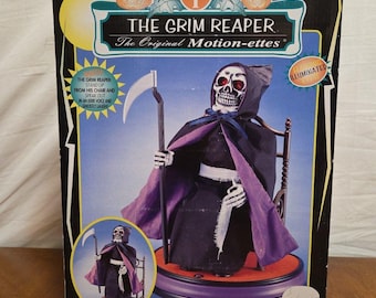 May include: A boxed Halloween decoration featuring "The Grim Reaper" motion-ette. The figure, with a skeletal face and hooded cloak, is seated and holds a scythe. The box has text that reads "The Grim Reaper The Original Motion-ettes" and "Illuminated".