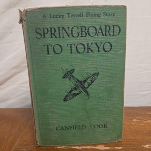 May include: A vintage book titled "Springboard to Tokyo" by Canfield Cook. The cover is green with black text and a black illustration of an airplane. The book is part of "A Lucky Terrell Flying Story" series.