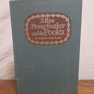 Puede incluir: Un libro antiguo titulado "Miss Pennyfeather and the Pooka" de Eileen O'Faolain. El libro tiene una cubierta de color verde azulado con una etiqueta ovalada marrón que muestra el título en escritura blanca. La etiqueta está enmarcada con un borde blanco decorativo.