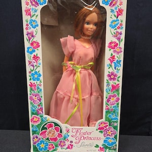 May include: A vintage Flower Princess Laurelle doll in its original box. The doll is dressed in a pink gown with a green ribbon and has long, flower-frosted hair. The box features floral designs and the text "Long and Beautiful Flower-Frosted Hair - easy to comb and style!"