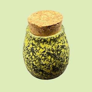 May include: A small, speckled jar with a cork stopper. The jar is a vibrant yellow with black speckles, and the cork is a light brown color. The jar has a rounded shape and a slightly textured surface.