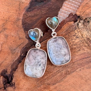 以下が含まれることがあります： ハート型のトップと長方形のボトムが付いた、銀色のイヤリングのペア。 ハート型のトップは青緑色で、長方形のボトムは白とグレーです。