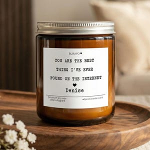 May include: A brown glass jar candle with a silver lid, sitting on a wooden tray. The candle has a white label with black text that reads "YOU ARE THE BEST THING I'VE EVER FOUND ON THE INTERNET" and the name "Denise".