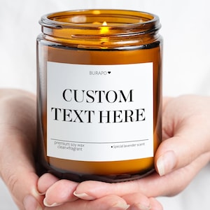Puede incluir: Una vela encendida en un tarro de vidrio color ámbar con una etiqueta blanca que dice "CUSTOM TEXT HERE". La etiqueta también incluye el texto "premium soy wax clean + fragrant" y "Special lavender scent."