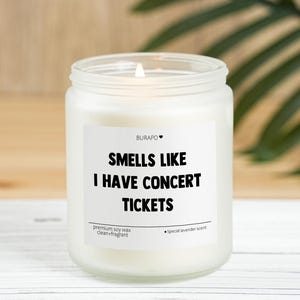 May include: A white candle in a glass jar with the text "SMELLS LIKE I HAVE CONCERT TICKETS". The candle has a special lavender scent and is made with premium soy wax.
