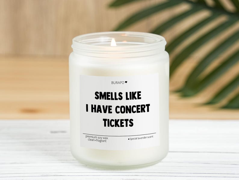 May include: A white candle in a glass jar with the text "SMELLS LIKE I HAVE CONCERT TICKETS". The candle has a special lavender scent and is made with premium soy wax.