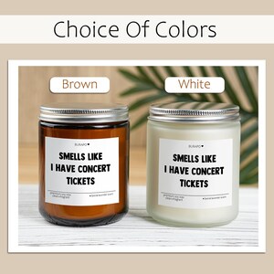May include: Two scented candles in glass jars with silver lids. One is brown, the other white. Each has a label that reads "SMELLS LIKE I HAVE CONCERT TICKETS". The text "Choice Of Colors" is at the top.