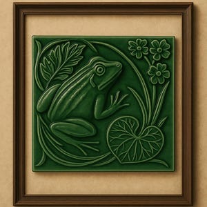 Puede incluir: Azulejo de cerámica verde con diseño de rana, enmarcado en un marco de madera marrón oscuro. La rana está rodeada de hojas, flores y un nenúfar. El azulejo cuadrado está montado sobre un fondo beige.