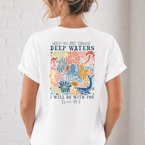 Könnte beinhalten: Ein weißes T-Shirt mit einer bunten Grafik auf der Rückseite, die einen Oktopus, einen Wal, eine Qualle, eine Meeresschildkröte und Blumen zeigt. Der Text lautet: WHEN YOU PASS THROUGH DEEP WATERS I WILL BE WITH YOU Isaiah 43:2 in Dunkelblau.