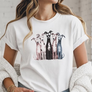Könnte beinhalten: Ein weißes T-Shirt mit kurzen Ärmeln und einer zentralen Grafikillustration von fünf Windhunden, die nebeneinander stehen. Die Hunde sind in verschiedenen Farben dargestellt, darunter Hellrosa, Weiß mit grauen Flecken, Schwarz, Braun und Dunkelgrau.