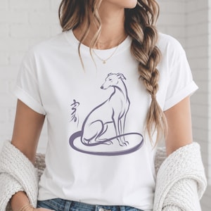 Może przedstawiać: Biały t-shirt z krótkim rękawem z fioletową ilustracją liniową charta siedzącego w okrągłej ramce. Po lewej stronie psa znajduje się stylizowany fioletowy symbol kaligraficzny. Wzór jest wyśrodkowany na przedniej części koszulki.