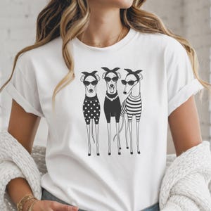 Könnte beinhalten: Ein weißes Kurzarm-T-Shirt mit einer schwarz-weißen grafischen Illustration von drei Windhunden, die Stirnbänder, Sonnenbrillen und verschiedene Outfits tragen, darunter ein gepunktetes Oberteil, ein einfarbiges mit Halskette und ein gestreiftes.