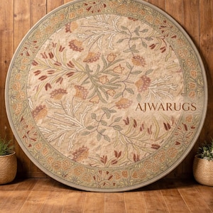 May include: A circular rug with a floral design and a green border. The rug has a beige background with a pattern of flowers and leaves in beige, brown, and green. The text "AJWARUGS" is displayed on the rug.