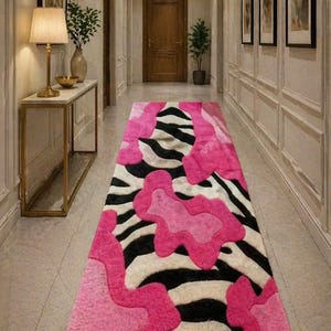 May include: A hallway runner rug with a bold design. The rug features a zebra stripe pattern in black and white, overlaid with bright pink organic shapes. The rug is rectangular and adds a pop of color to the neutral hallway.