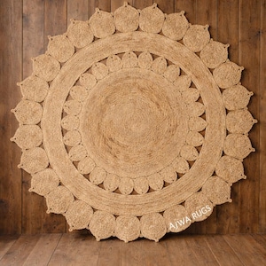 Könnte beinhalten: Runder Jute-Teppich mit floralem Design. Der Teppich hat eine natürliche beige Farbe und ein kreisförmiges Muster mit detailliertem Rand. Der Text "AJWA RUGS" ist unten rechts zu sehen.