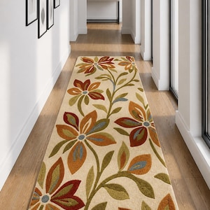 Könnte beinhalten: Ein beigefarbener Blumenschläufer mit großen stilisierten Blumen in Orange-, Rot-, Grün- und Blautönen. Der Teppich liegt in einem Flur mit Holzböden und weißen Wänden. Das Design des Teppichs zeigt ein sich wiederholendes Blumenmuster.