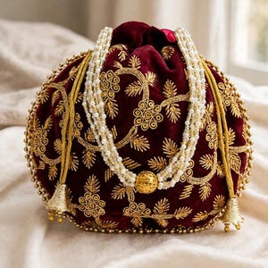 May include: A deep burgundy velvet drawstring pouch featuring intricate gold thread embroidery in floral patterns. The bag is adorned with a multi-strand white pearl handle and gold tassels at the base. The text ThePurseGallery is visible.