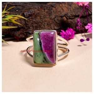 Può includere: Anello d'argento con una pietra rettangolare divisa in sezioni verdi e viola. L'anello ha un design a doppia fascia. Il testo "JewelryjonesandJames" è visibile sull'anello.