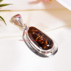 May include: A silver pendant with a large, oval-shaped, brown gemstone. The gemstone has a unique pattern of dark and light brown inclusions. The pendant is set in a polished silver frame and has a silver bail.