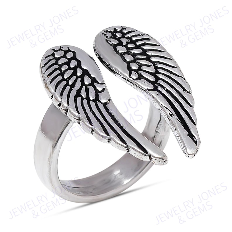 Puede incluir: Un anillo plateado con un dise&ntilde;o abierto, con dos alas de &aacute;ngel estilizadas. Las alas tienen patrones de plumas grabadas y la banda del anillo es lisa y pulida. Esta joya es un accesorio decorativo.