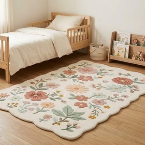 Può includere: Un tappeto rettangolare con bordo smerlato, fondo color crema e un motivo floreale nei toni del rosa polvere, verde salvia e giallo tenue. Il tappeto presenta vari fiori, steli e foglie distribuiti su tutta la superficie.