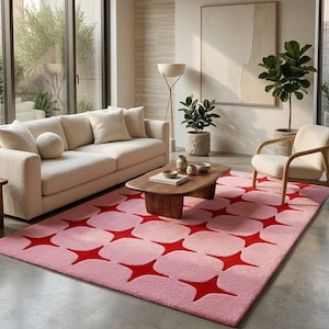 May include: A rectangular area rug featuring a repeating geometric pattern of soft pink rounded squares interspersed with vibrant red four-pointed star shapes. The rug has a textured pile surface and covers a portion of the floor in the room.