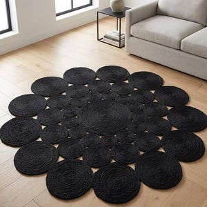 May include: A large, circular area rug composed of numerous smaller, interconnected black woven circles of varying sizes. The rug features a textured, coiled rope-like construction, creating a dense, floral-inspired pattern across the entire surface.