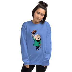 Puede incluir: Sudadera azul claro con un personaje de dibujos animados que se quita el sombrero marrón. El personaje lleva una chaqueta verde, pantalones negros y un bastón. La sudadera es de color azul claro liso.