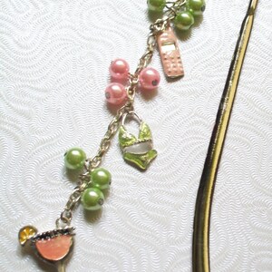 May include: A silver-toned charm bracelet with a cocktail, bikini, and cell phone charm. The bracelet also features pink and green beads. The cocktail charm has an orange slice and the bikini is green and white.