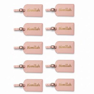 May include: A collection of ten pink luggage tags. Each tag has a rectangular shape with rounded corners and a small strap with a buckle. The word "Bismillah" is printed in gold lettering on each tag.