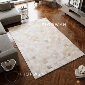 Può includere: Un tappeto rettangolare con un design patchwork nei toni del crema, beige e marrone chiaro. Il tappeto è composto da quadrati e riporta la scritta FIORWYN. Il tappeto è posato su un pavimento in legno.