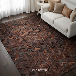 Può includere: Un tappeto rettangolare con un motivo geometrico nei toni del marrone, beige e grigio. Il tappeto è posato su un pavimento in legno scuro, con un divano bianco e un tavolino sullo sfondo. Il tappeto ha la scritta FIORWYN.