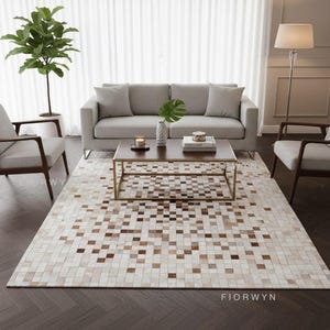 May include: A living room scene featuring a light gray sofa, a brown coffee table with a gold frame, and two armchairs. A large area rug with a mosaic pattern of brown and cream squares covers the floor. A floor lamp and a potted plant are also visible.