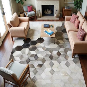 Könnte beinhalten: Ein Wohnzimmer mit einem geometrisch gemusterten Teppich in Grau-, Schwarz- und Weißtönen. Der Teppich ist der Mittelpunkt, ergänzt durch pfirsichfarbene Sofas und Sessel sowie einen Holztisch. Der Raum hat einen Kamin und Holzböden.