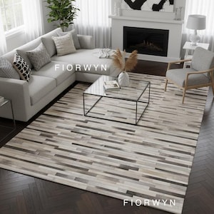 May include: A rectangular area rug with a striped pattern in shades of gray, beige, and brown. The rug is placed on a dark wood floor. The word "FIORWYN" is printed on the rug.
