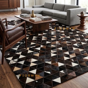May include: A large area rug featuring a geometric pattern of triangles in various shades of black, brown, white, and tan. The rug is constructed from individual pieces of cowhide leather, creating a textured surface with the text FIORWYN visible.