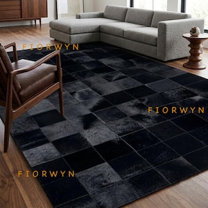 May include: A large rectangular area rug featuring a patchwork design of square black and dark gray hide tiles. The rug displays a repeating grid pattern with the text FIORWYN printed in yellow across three different sections of the surface.