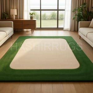 May include: A rectangular rug with a cream-colored center and a vibrant green border. The rug is placed on a hardwood floor in a living room setting, with two sofas and a window in the background. The text "HASHIRRUGS" is visible on the rug.